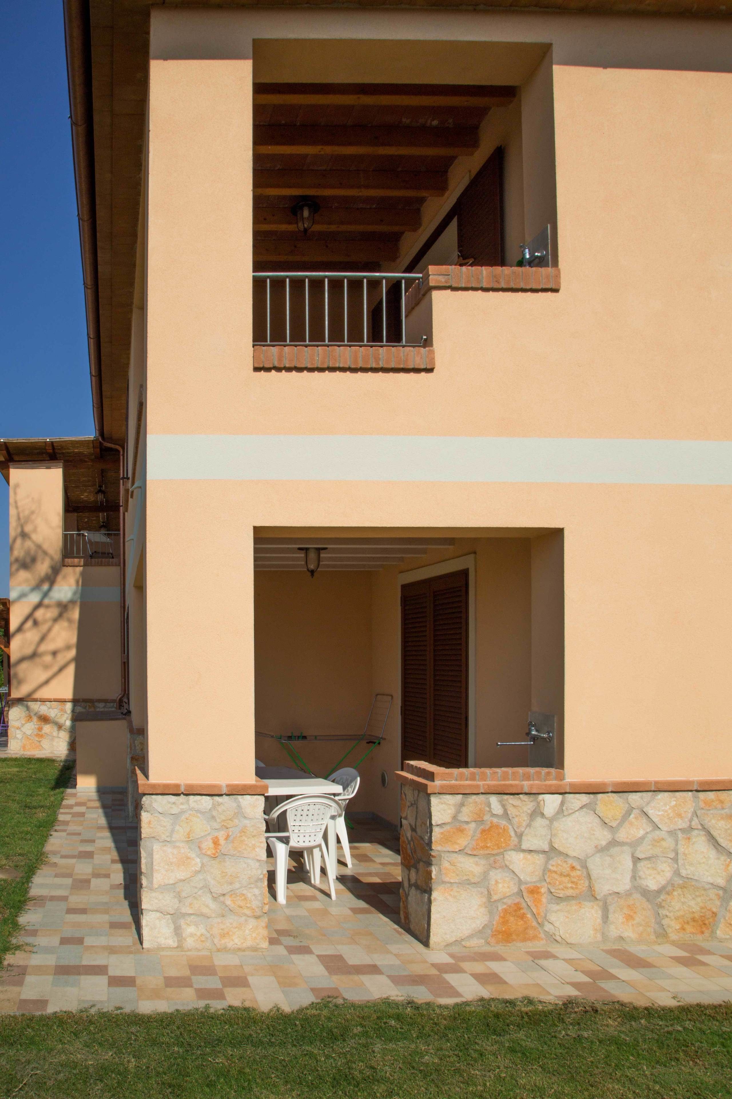 A two-story building with a stone and tiled patio area, a balcony, and a door leading to an interior space.