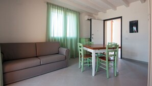 A living room with a sofa, a dining table with chairs, a window with curtains, and a door. - La Residenza del Golfo (Scarlino)
