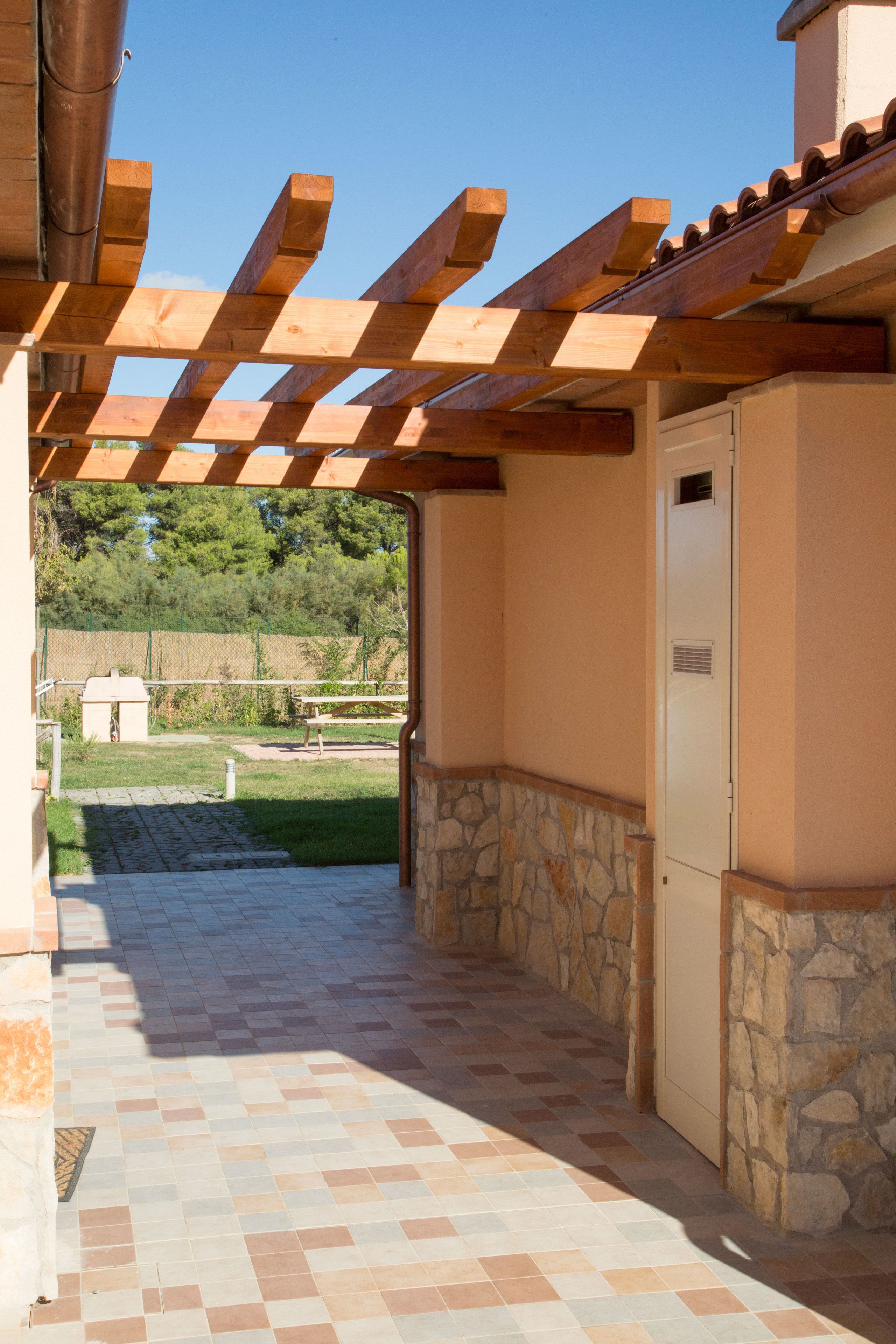 A covered outdoor area with a stone wall and a tiled floor leading to a building entrance.