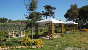 A garden with two wooden gazebos, a barbecue setup, and a paved area with a picnic table. - La Residenza del Golfo (Scarlino)