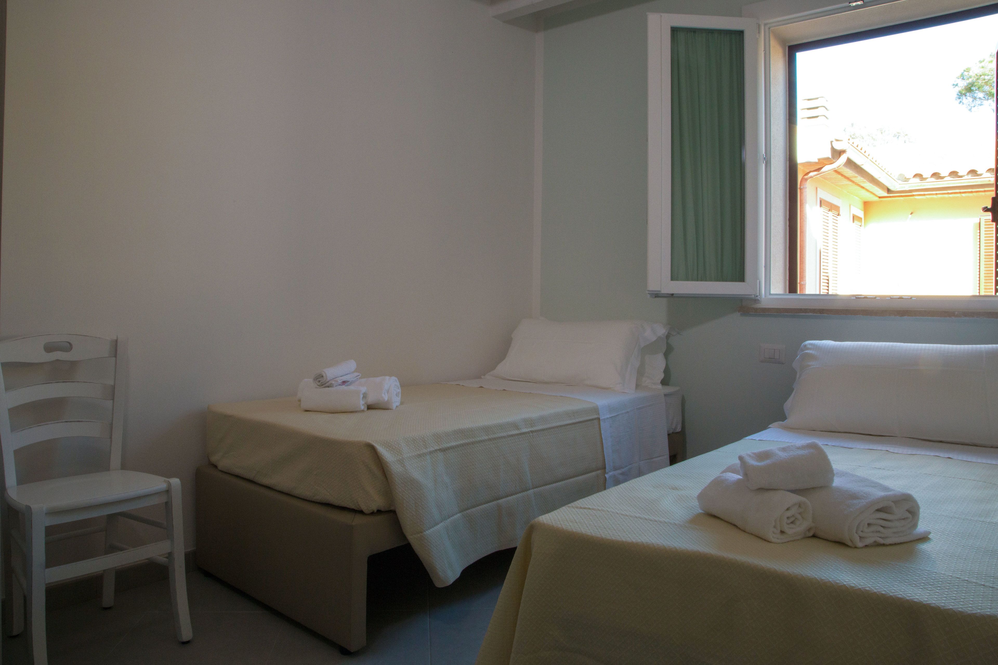 A hotel room with two single beds, a chair, and a window with a view of a building.