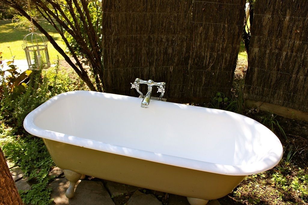 Eine Freiluftbadewanne im Vintage-Stil, umgeben von Grünpflanzen und einem Holzzaun.