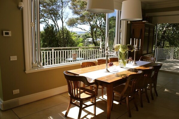A dining area with a large window, a wooden table, and chairs. - 970 Lonely Bay Lodge (Cooks Beach)