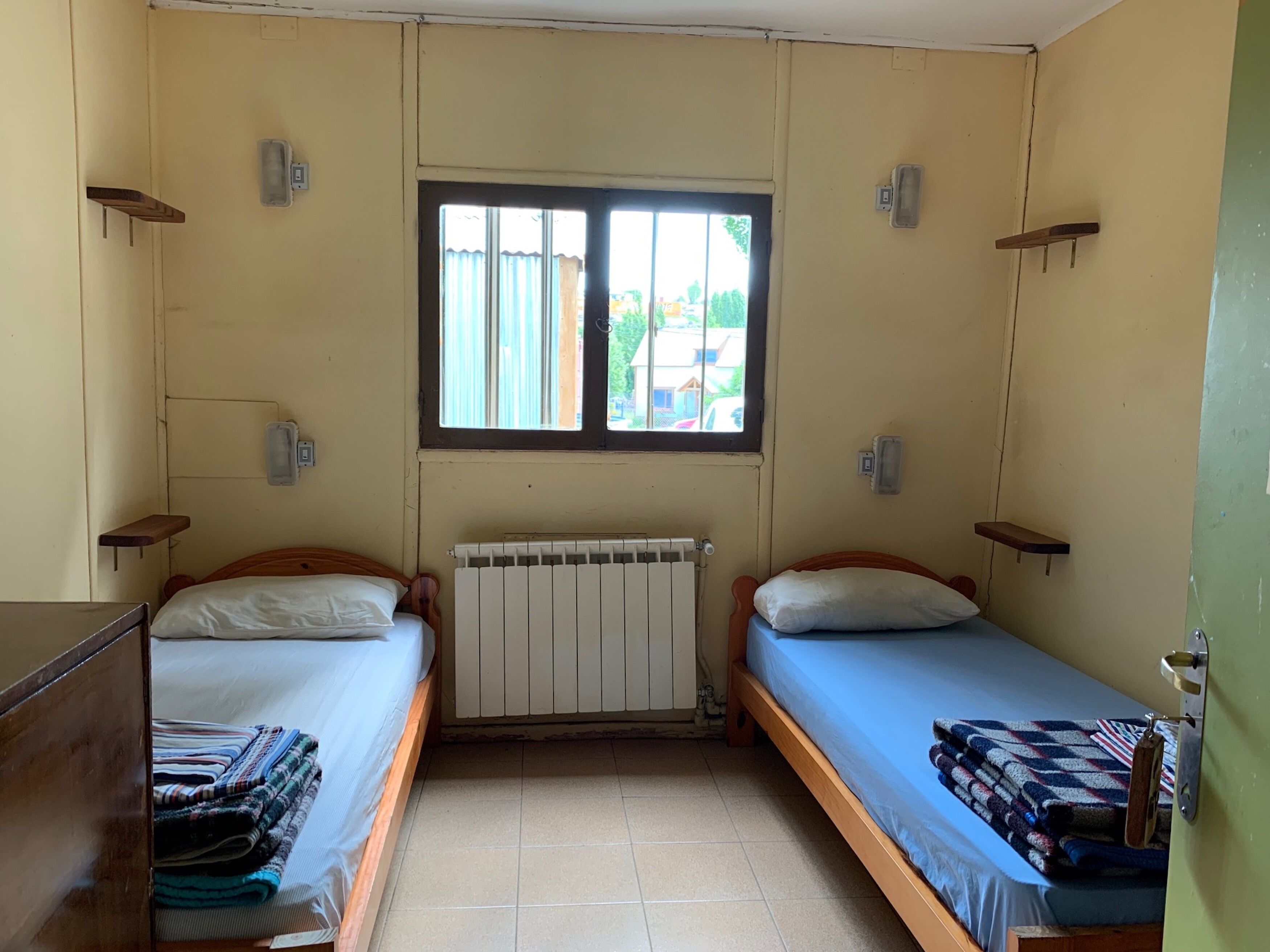 Una habitación pequeña y sencilla con dos camas individuales, una ventana y un radiador.