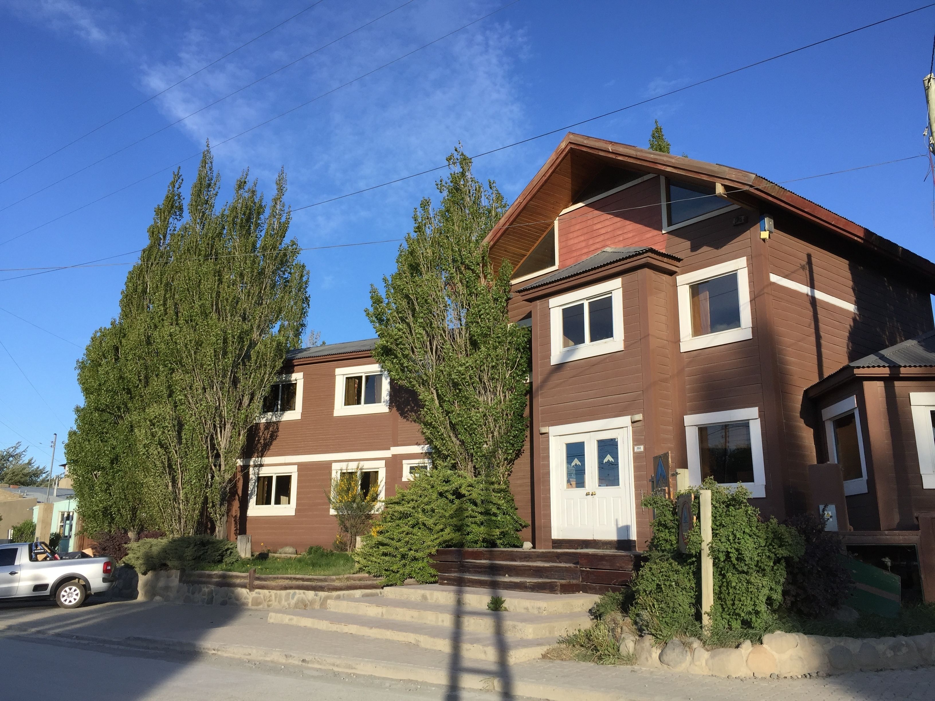 A two-story residential building with a brown exterior and white trim, surrounded by trees and a parked car.
