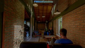 A cozy interior with brick walls, wooden ceiling beams, and hanging pendant lights. There are leather chairs and a table in the center. - Hostel del Glaciar Pioneros (El Calafate)