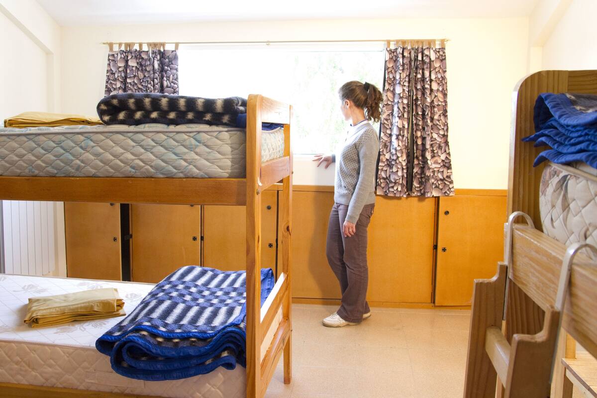 Une chambre de dortoir avec des lits superposés, une fenêtre avec des rideaux et une armoire en bois.