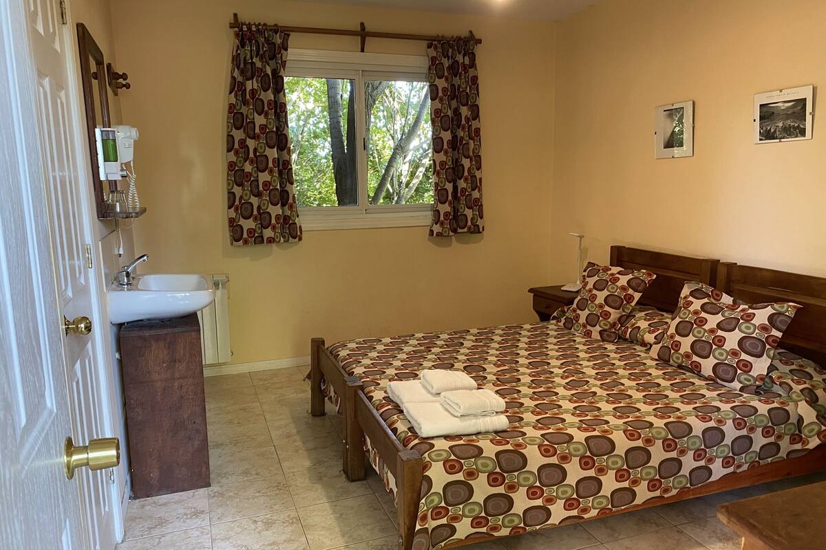 Une chambre à coucher comprenant un lit, une table de chevet, une commode, une fenêtre avec des rideaux, un lavabo et un miroir.