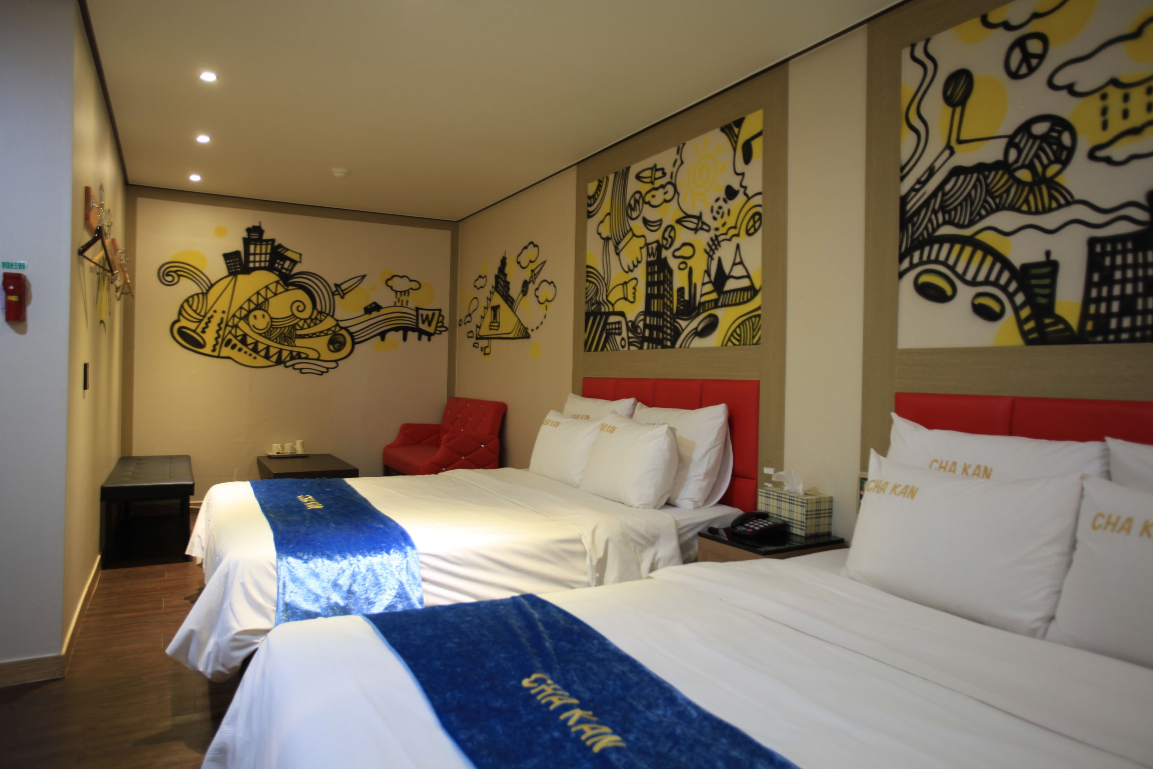 Una habitación de hotel con dos camas, una silla roja y un mural en la pared.