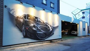 A mural of a sports car on a building wall, a hotel sign, and a parking garage entrance.