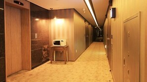 A hotel hallway with wooden doors, a microwave on a small table, and a carpeted floor.