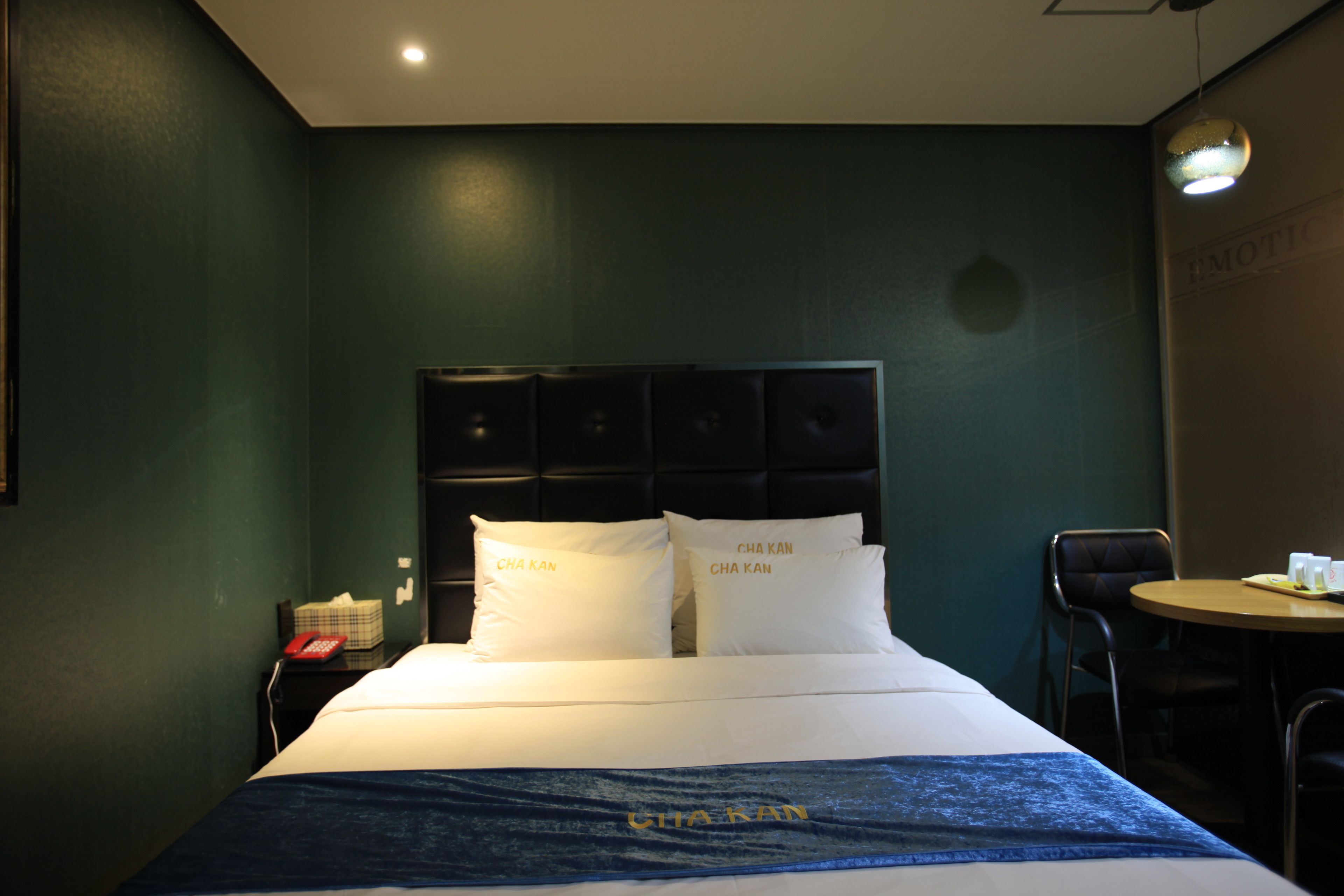 A hotel room with a bed, a bedside table with a telephone, and a small table with cups and a tray.