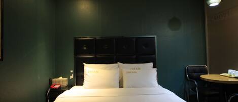 A hotel room with a bed, a bedside table with a telephone, and a small table with cups and a tray.