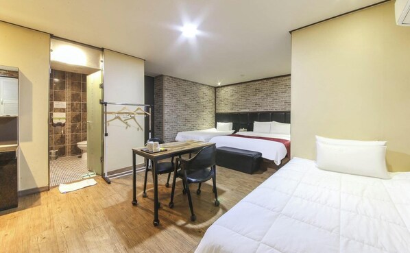 Habitación de hotel con dos camas, un escritorio con silla, una mesita pequeña, un armario y una pared de ladrillo.
