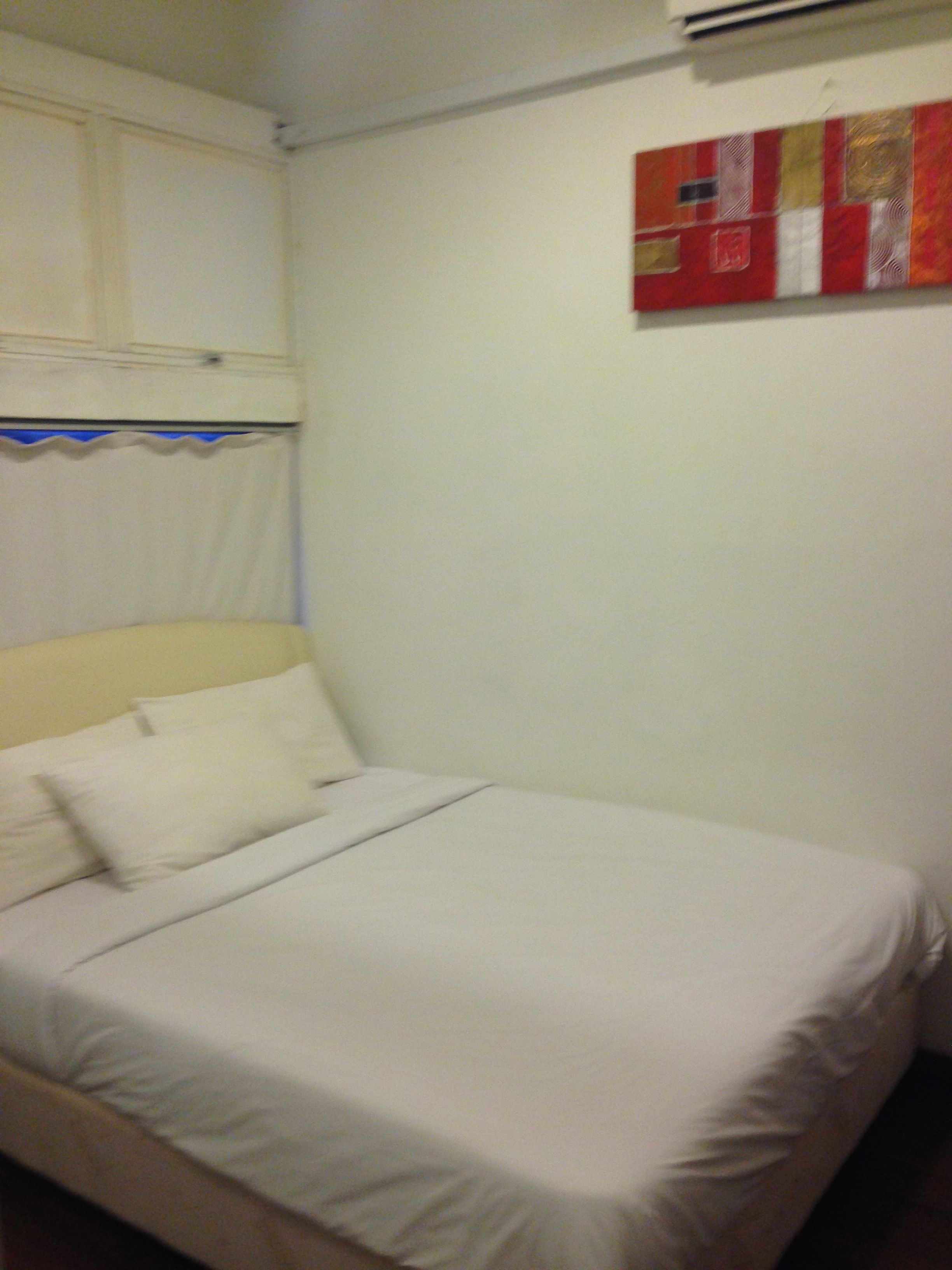 Een bed met witte lakens, een hoofdbord, en een wand met kunstwerk in rood-wit patroon.