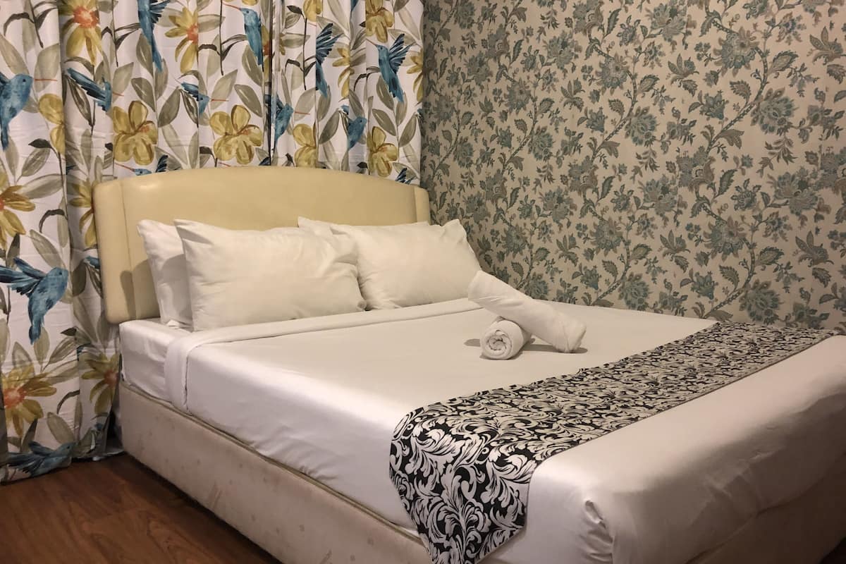 A neatly made bed with white linens, a rolled towel, and a black and white patterned throw.