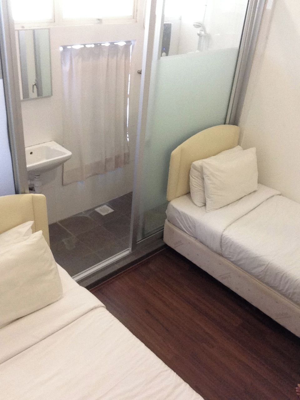 A small, single-room accommodation with a bed, a bedside table, a mirror, and a shower area.