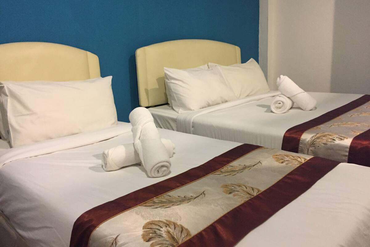 Two single beds with white linens and pillows, a blue wall, and a red decorative border on the beds.