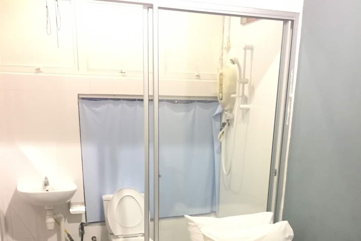 A compact hotel room with a shower, toilet, sink, and a bed with a rolled towel.