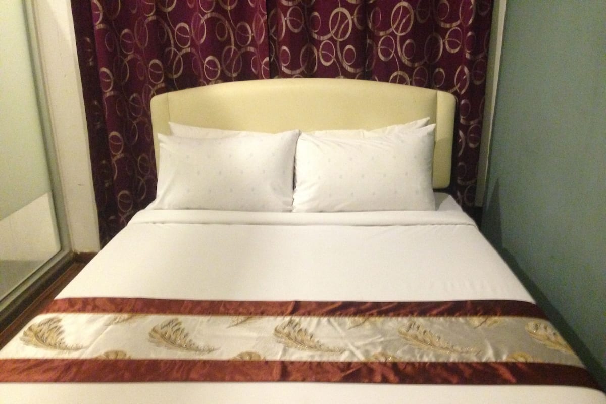A hotel room with a bed, pillows, and a patterned bedspread.