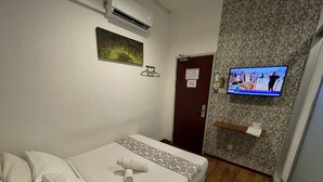 Habitación de hotel con cama, televisión montada en la pared, aire acondicionado y una puerta con un letrero.