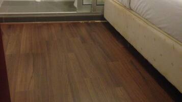 Una habitación con piso de madera, una cama con ropa de cama blanca, un inodoro y una zona de ducha.