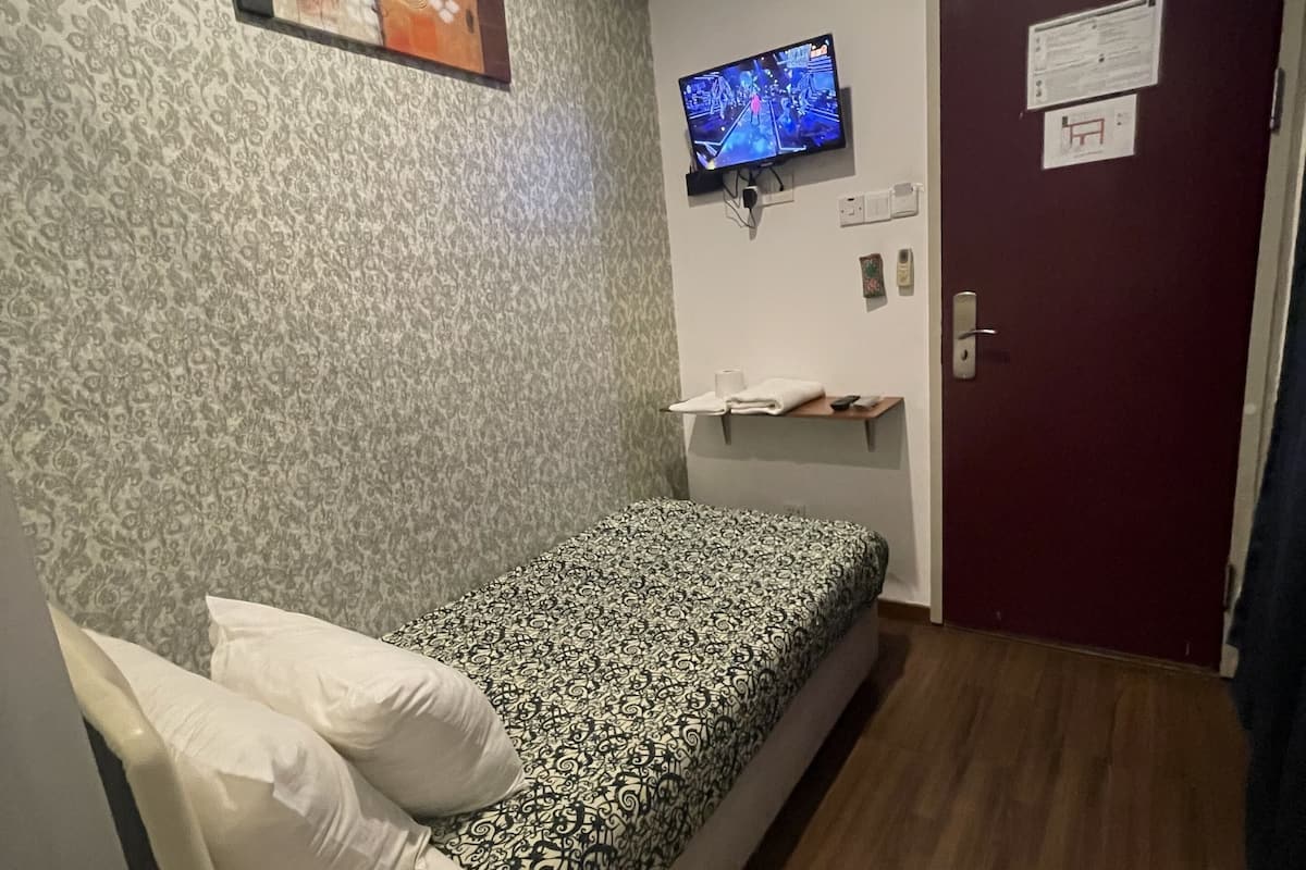 A small, single-bed room with a patterned bedspread, a television mounted on the wall, and a door with a sign.