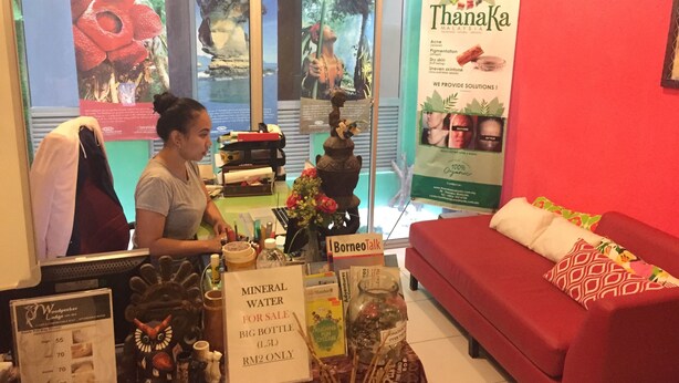 Una habitación con un sofá rojo, exhibición de agua mineral para la venta y un cartel publicitario de Thanaka.