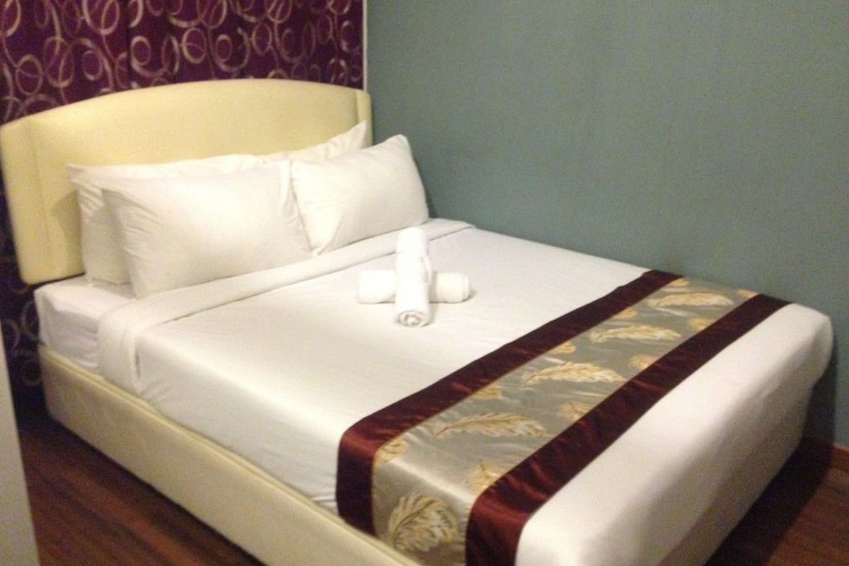 A neatly made bed with white linens, a decorative headboard, and a floral-patterned bedspread.
