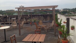 Un patio en la azotea con muebles de madera, plantas en macetas e iluminación colgante.