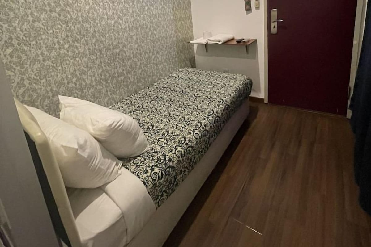 Une petite pièce avec un lit, un téléviseur fixé au mur, une porte avec une pancarte et un papier peint à motifs.