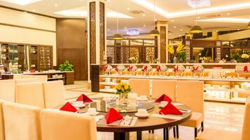 Une salle à manger bien éclairée, avec des tables rondes dressées pour le service, agrémentée de serviettes rouges et d’un arrangement floral central.