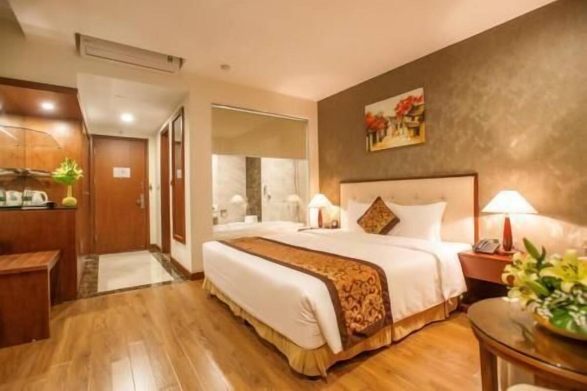 A hotel room with a bed, bedside table, lamp, and a mirror.