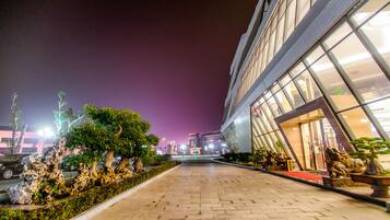 A nighttime view of a building with a paved walkway, trees, and decorative statues.