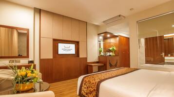 A hotel room with a bed, a desk, a chair, a small table with a vase of flowers, a mirror, and a sign with text.