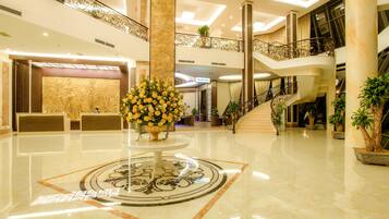 A spacious lobby with a marble floor, a central floral arrangement, and a staircase leading to upper levels.
