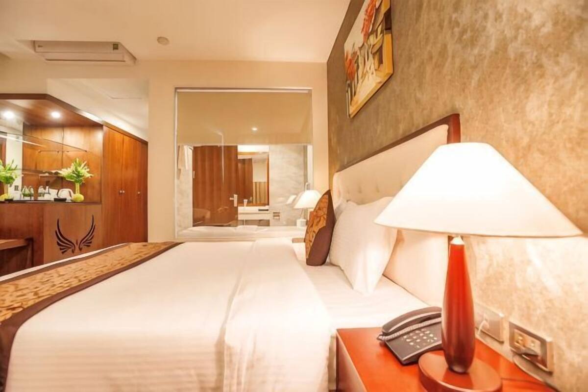 A hotel room with a bed, bedside table with a lamp, a telephone, a desk with a computer, and a mirror.