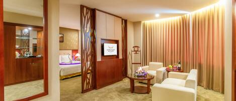 Habitación de hotel con cama, televisor, zona de estar con mesa y un espejo grande.