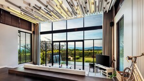 A modern living room with a large window, a sofa, a TV, and a bicycle. - The Private Pool Villas at Civilai Hill Khao Yai (Pak Chong)