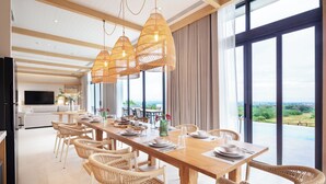 A spacious dining area with a long wooden table, wicker chairs, and pendant lights. - The Private Pool Villas at Civilai Hill Khao Yai (Pak Chong)