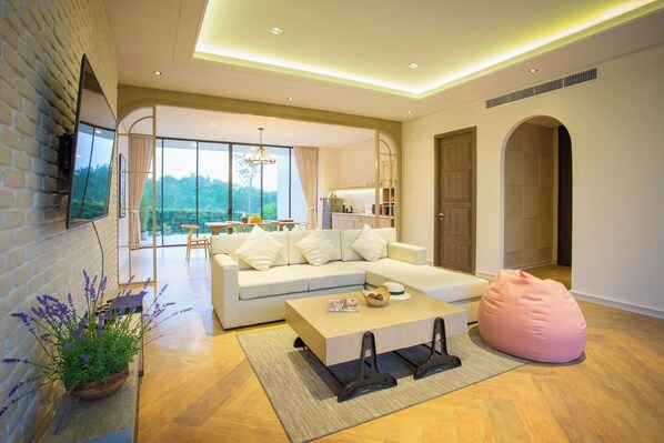 Una sala de estar moderna con sofá, mesa de centro y un sillón inflable rosa. Hay un televisor montado en la pared de ladrillo, y un ventanal ofrece vistas al exterior.