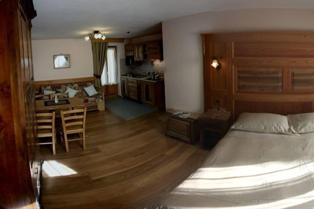 A cozy room with a wooden bed, a small desk, and a kitchenette.