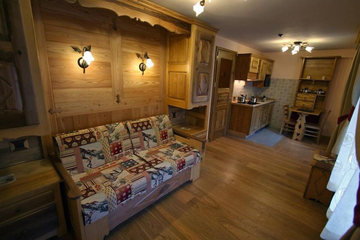 A cozy living room with a wooden sofa, wooden cabinets, and a kitchen area in the background.