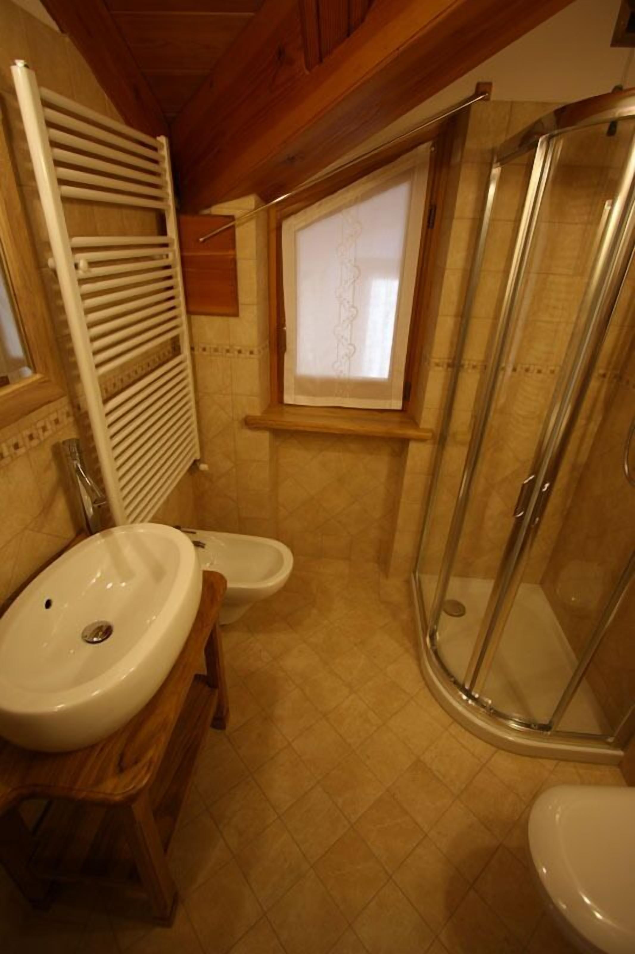 Un baño con tocador de madera, lavamanos, inodoro, cabina de ducha y ventana con vistas.