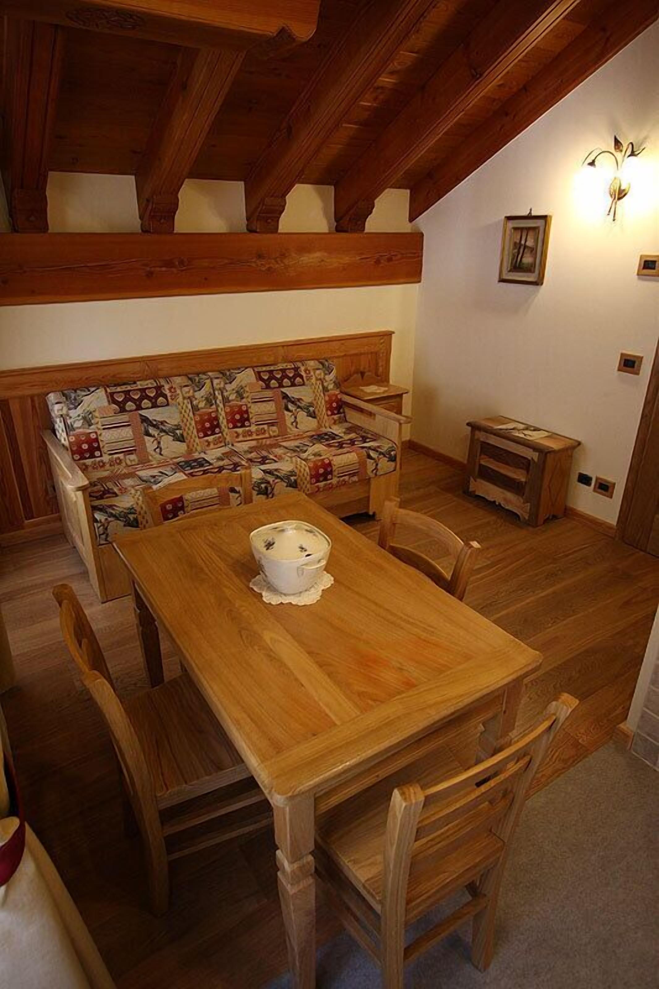 A wooden dining table with four chairs, a bench with patterned cushions, and a small wooden side table.