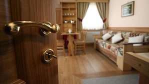 Une porte en bois avec une poignée en laiton, une table à manger en bois avec des chaises, un canapé agrémenté de coussins à motifs floraux et une bibliothèque dans une pièce chaleureuse.