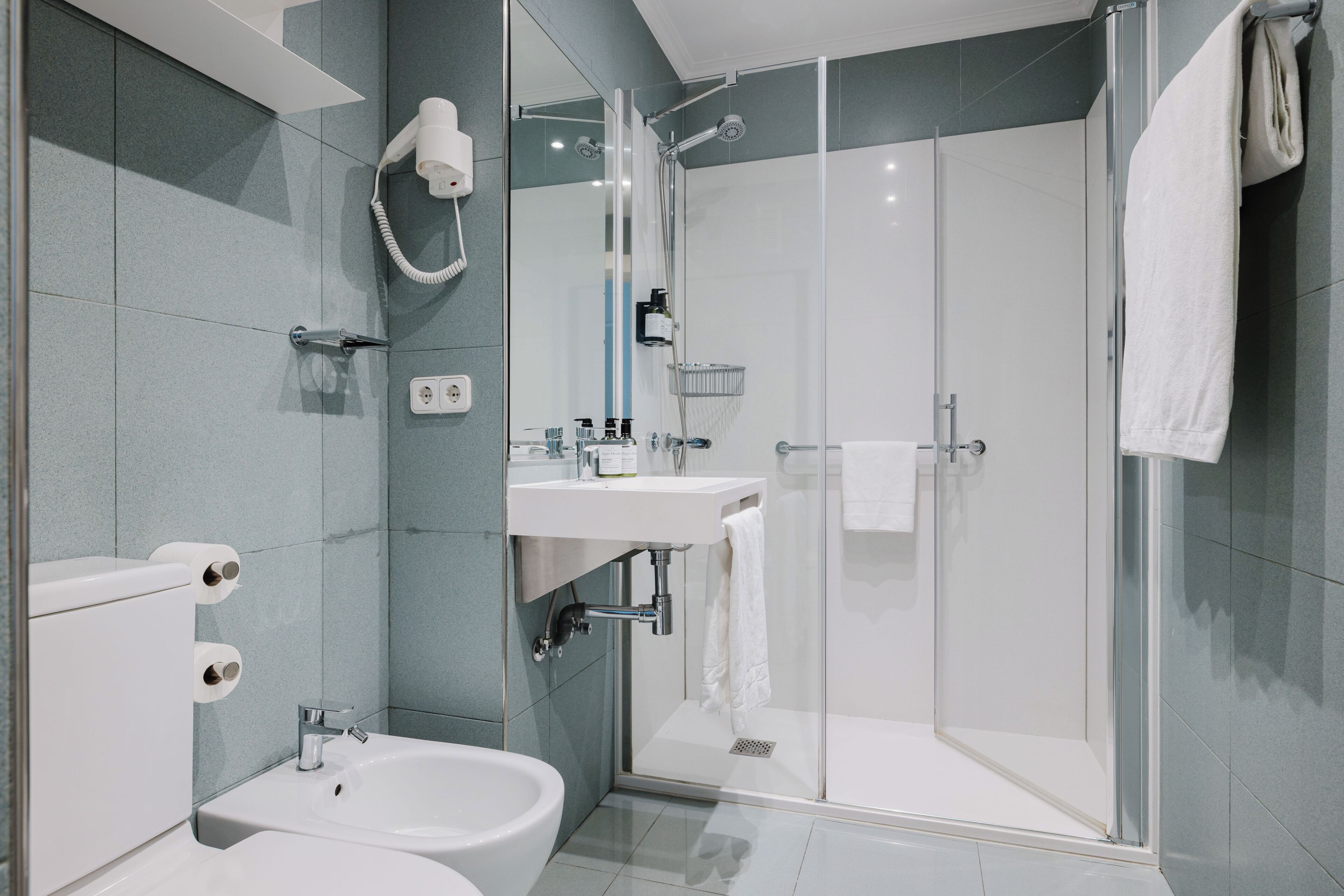 A modern bathroom with a glass-enclosed shower, a sink, and a bidet.