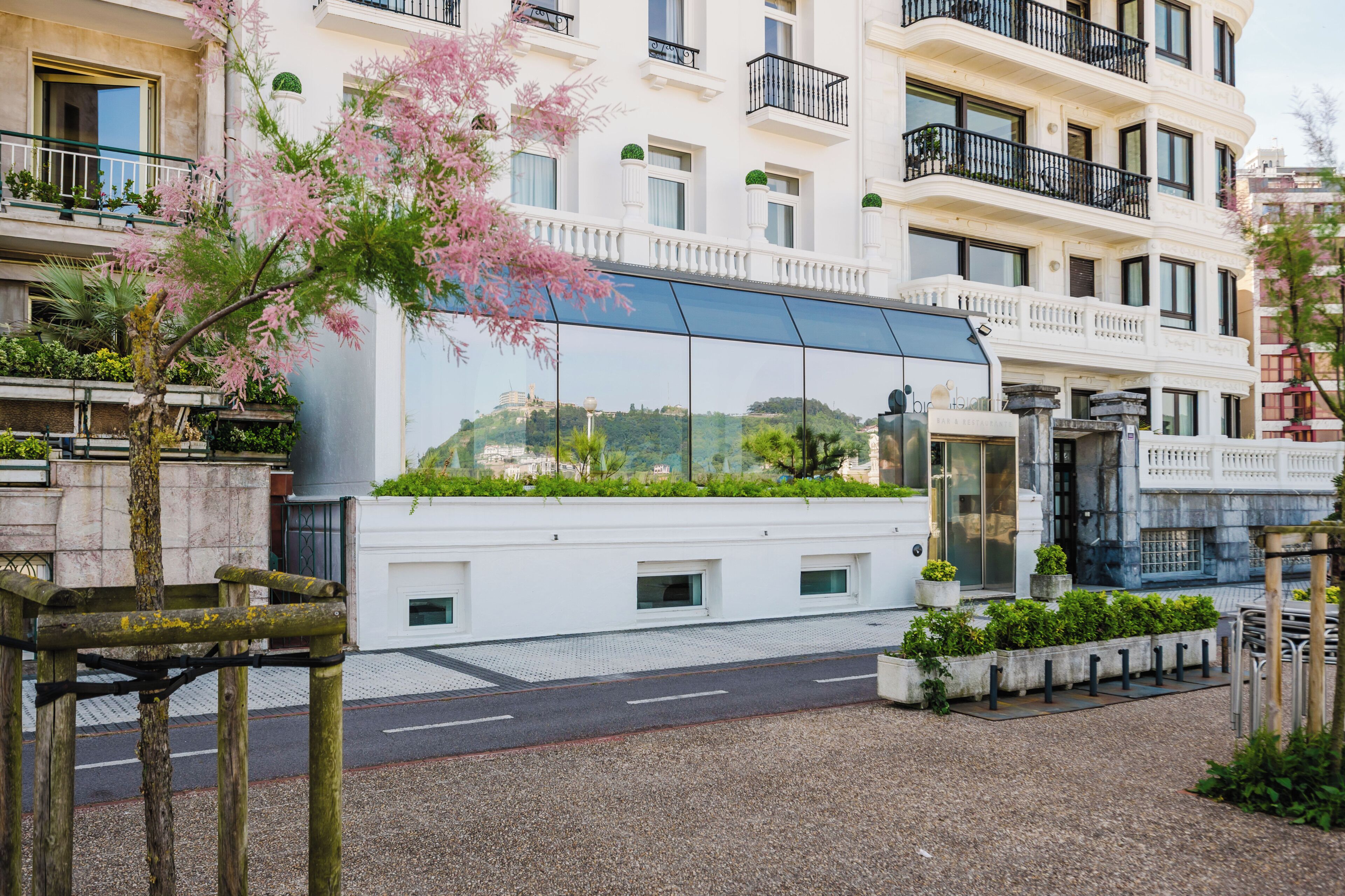 A modern building with balconies, a glass facade, and a garden area.