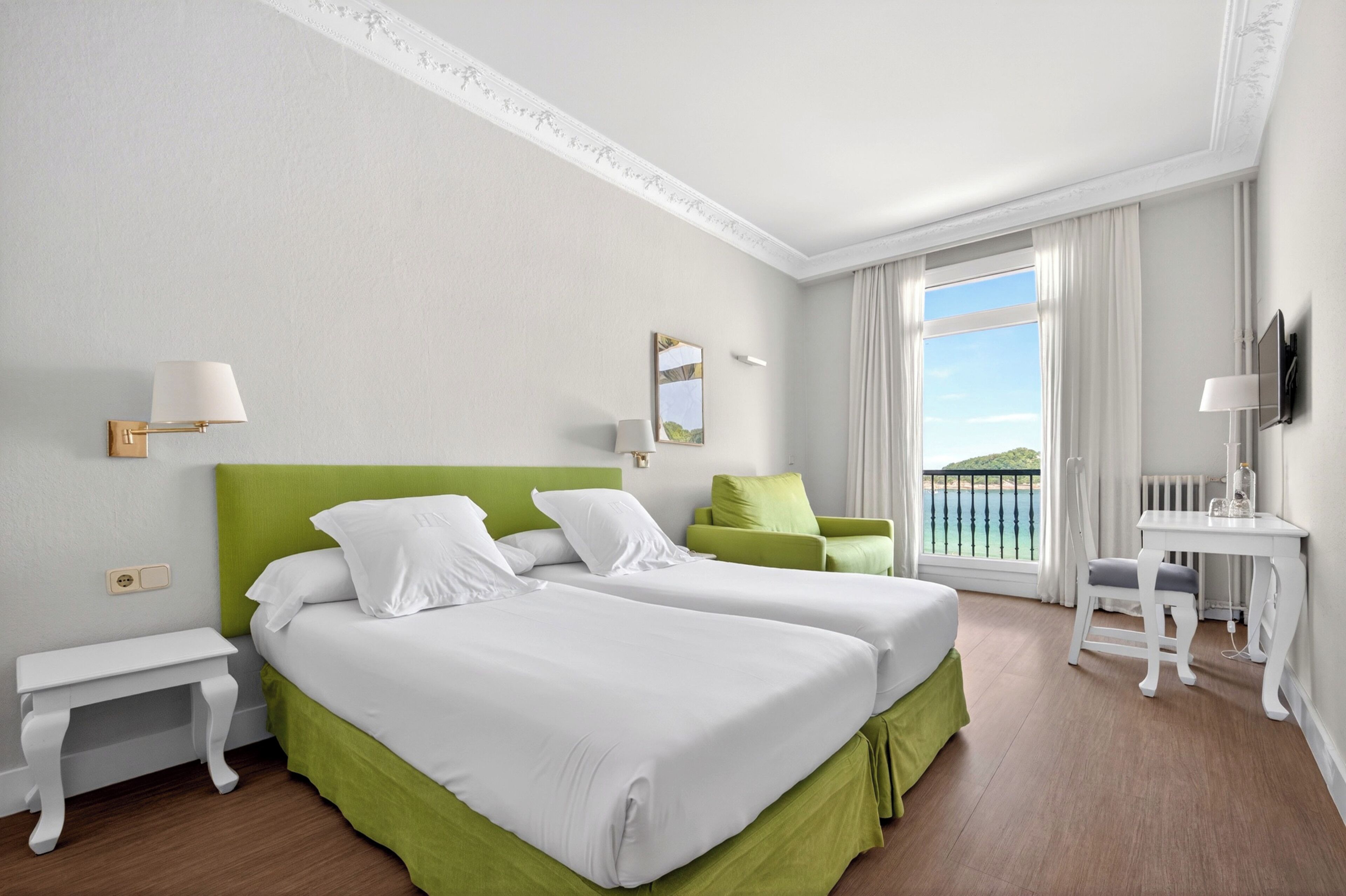 A hotel room with two beds, a desk, a chair, a TV, and a window with a view.