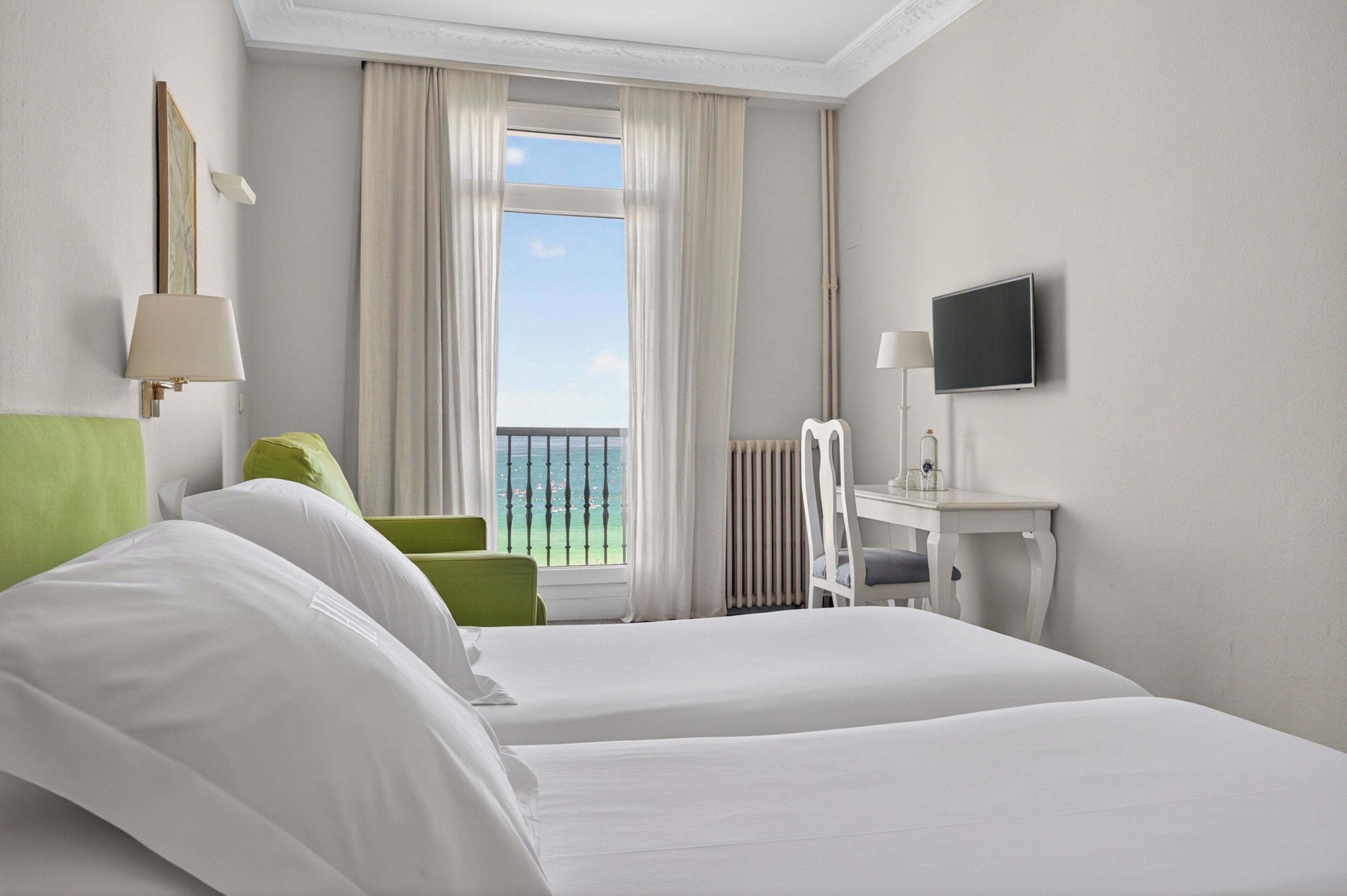 Une chambre d’hôtel avec deux lits, un bureau, une chaise, une télévision et une vue sur la mer.
